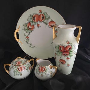 Könnte beinhalten: Ein Vintage-Porzellan-Tee-Set mit einem grün-weißen Blumendesign mit roten Mohnblumen. Das Set beinhaltet eine Teekanne, eine Milchkännchen, eine Zuckerdose und eine große Servierplatte mit Griffen. Das Set ist mit goldenen Akzenten verziert.