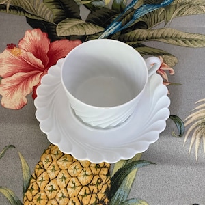 May include: A white teacup and saucer set with a scalloped edge. The saucer has a swirl design.