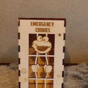 Könnte beinhalten: Eine Holz-Keksdose mit einem Ausschnitt von Cookie Monster hinter Gittern. Die Dose ist mit "Emergency Cookies" beschriftet.