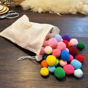 May include: A white drawstring bag filled with colorful pom poms. The pom poms are in various shades of pink, blue, green, yellow, orange, and red.