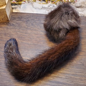 May include: A brown fur tail with a brown fur pom-pom on the end. The tail is curled into a circle shape.