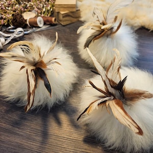 May include: Three fluffy white pom-poms with brown and white feathers attached. The pom-poms are arranged on a wooden surface.