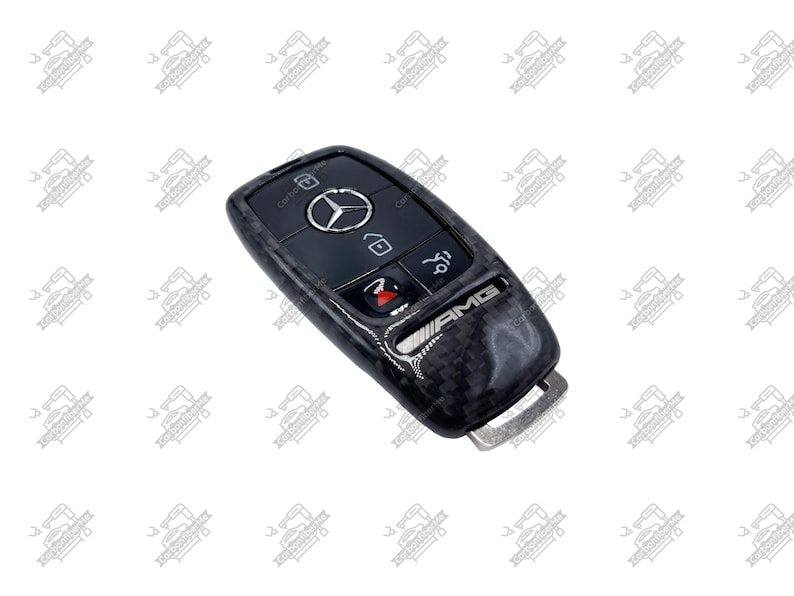 May include: A black and carbon fiber Mercedes-Benz car key with the AMG logo. The key has several buttons, including a lock, unlock, and trunk release. The Mercedes-Benz logo is in the center.