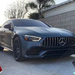May include: A gray luxury car with a black grille and black wheels is parked on a concrete driveway. The car has the Mercedes-Benz logo on the front. Two car keys are in the foreground.
