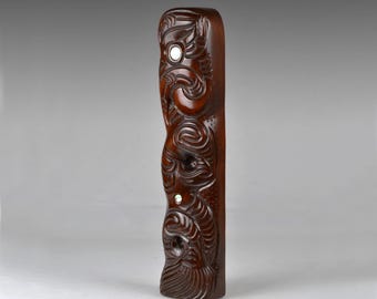 May include: A dark brown wooden carving with intricate details. The carving features a repeating pattern of stylized figures with rounded features. The carving is smooth and polished.