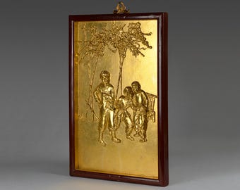 May include: A rectangular gold-colored relief artwork depicting a scene with figures under a tree. The artwork is framed in a dark brown wooden frame. The relief is detailed and shows multiple figures in a scene.