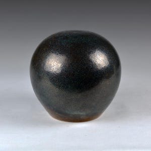Peut inclure: Un vase sphérique en céramique sombre avec une surface texturée. Le vase a un éclat métallique avec des reflets bleus et bruns. La forme ronde et la couleur sombre lui confèrent une esthétique moderne et minimaliste. Le vase est adapté à la décoration intérieure.