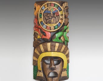 May include: A colorful wooden mask with a central face surrounded by a circular design. The mask is decorated with intricate carvings and painted in shades of red, green, yellow, and blue. The central face has a serious expression with closed eyes and a wide mouth.