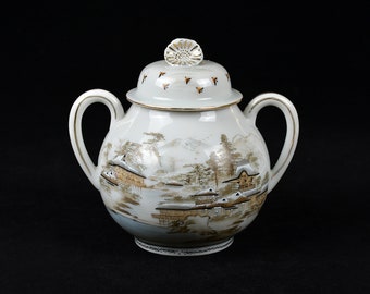 May include: White porcelain sugar bowl with a lid and two handles. The bowl is decorated with a Japanese-inspired landscape scene in shades of brown and gold.