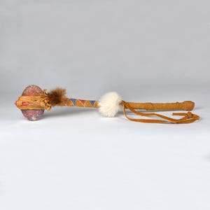 May include: A Native American ceremonial war club with a stone head wrapped in leather and decorated with red, blue and yellow paint. The handle is wrapped in leather and has a white fur pom-pom.