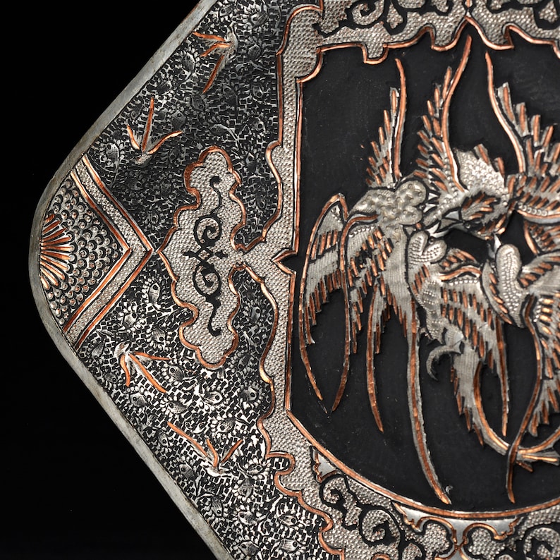 May include: A silver and copper tray with an intricate design of birds and clouds. The tray is square and has a black background.