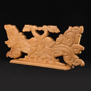 May include: A wooden sculpture of two peacocks with their tails spread out. The sculpture is intricately carved with details on the feathers and the birds' bodies. The sculpture is mounted on a wooden base.