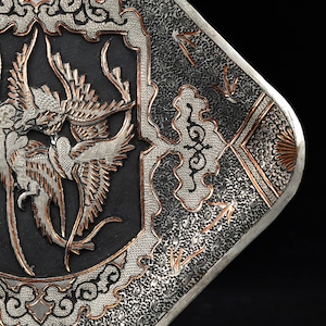 May include: A silver and copper tray with an intricate design of birds and floral motifs. The tray has a black background and is decorated with a raised, textured pattern.