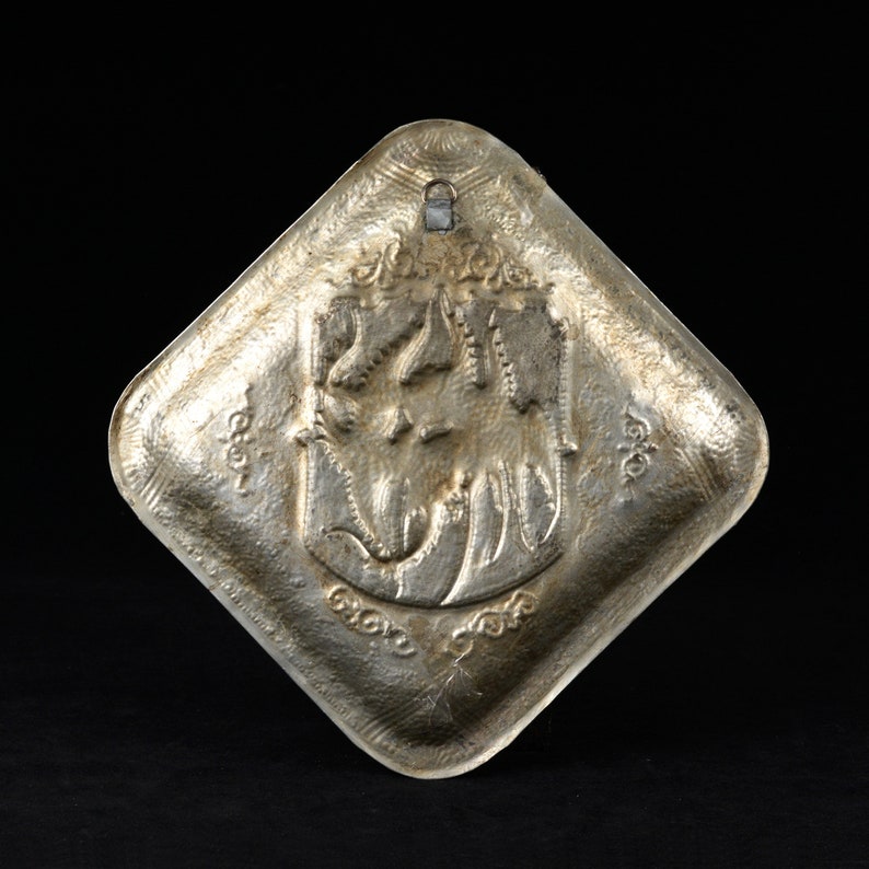 May include: A silver, diamond-shaped decorative plate with an embossed design of a stylized animal with a floral motif. The plate has a hanging loop at the top.