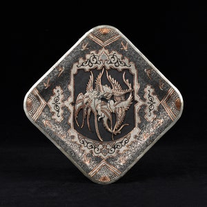 May include: A silver and copper square tray with a raised design of two birds in flight. The tray has a black background and intricate details in silver and copper.