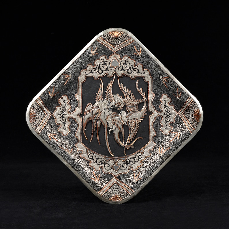 May include: A silver and copper square tray with a raised design of two birds in flight. The tray has a black background and intricate details in silver and copper.