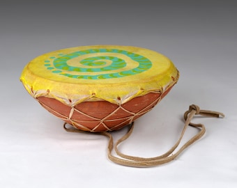 May include: A small, yellow hand drum with a green and blue spiral design. The drum has a brown leather strap.