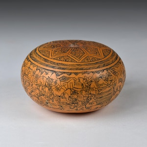 Puede incluir: Una calabaza redonda y naranja con intrincados diseños negros grabados. La tapa presenta un patrón de estrella, mientras que el cuerpo representa una escena detallada de personas y edificios. Esta calabaza decorativa es una obra de arte única.