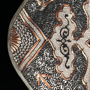 May include: Close-up of a silver tray with intricate copper and silver designs. The tray has a geometric pattern with a floral motif in the center.
