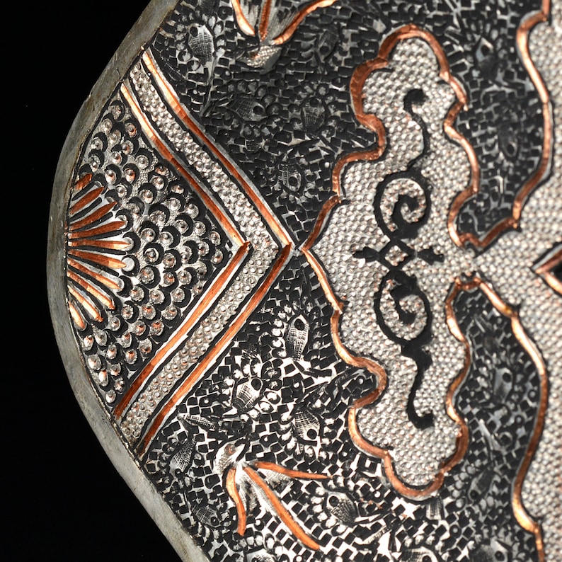 May include: Close-up of a silver tray with intricate copper and silver designs. The tray has a geometric pattern with a floral motif in the center.