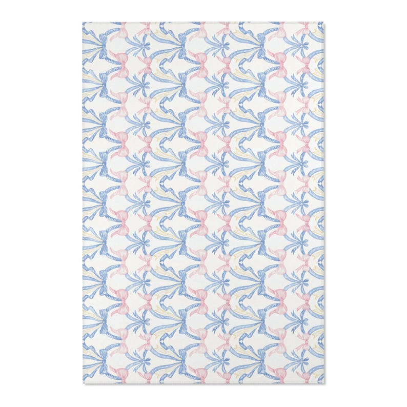 May include: A rectangular rug with a repeating pattern of blue and yellow ribbons and pink bows on a white background. The design is symmetrical and creates a delicate, decorative effect. The rug is suitable for a bedroom or living room.