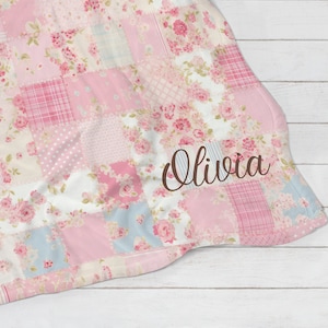 May include: A pink and blue patchwork fleece blanket with a floral pattern and the name "Olivia" embroidered on it.