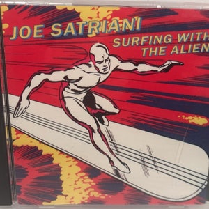May include: A CD case with a red, yellow, and blue comic book style illustration of a silver figure surfing on a white surfboard. The text "JOE SATRIANI SURFING WITH THE ALIEN" is printed on the case.