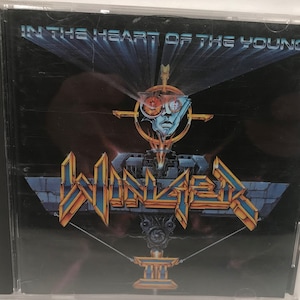 May include: A CD case with a black background and a blue and gold graphic of a band called "Winger" with the text "In the Heart of the Young" and "III" on the front.