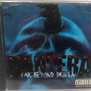May include: A CD case with a blue and black image of a skull with a metal spike on top. The text "Pantera" and "Far Beyond Driven" are printed in red and black on the front of the case. A parental advisory sticker is in the bottom right corner.