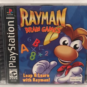 May include: A PlayStation game case for Rayman Brain Games. The case is blue with a picture of Rayman, a cartoon character with red and white clothing, on the front. The text "Leap & Learn with Rayman!" is printed on the case.