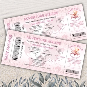 May include: Two pink baby shower invitations designed as airline tickets. The tickets read "Adventure Airline" and include details like the date, time, and destination. A small illustration of a teddy bear in a plane is on the right side.