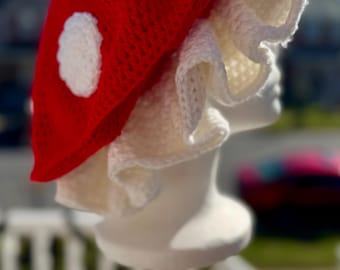 May include: A red crocheted mushroom hat with white crocheted ruffles and white polka dots.
