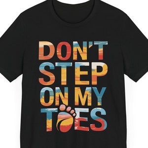 May include: Black t-shirt with a colorful graphic that says "Don't Step On My Toes" with a footprint graphic.