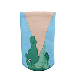 May include: A light blue sock featuring a graphic illustration of a green crocodile with its mouth open, biting into a large, tan-colored triangular shape that resembles a slice of pizza or a cone, with a small logo near the bottom edge.