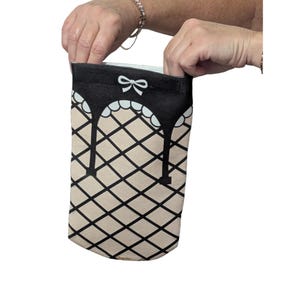May include: A rectangular fabric pouch featuring a beige background with a black diamond grid pattern. The top section is solid black with a white scalloped trim and a small white bow graphic centered near the top edge of the pouch.