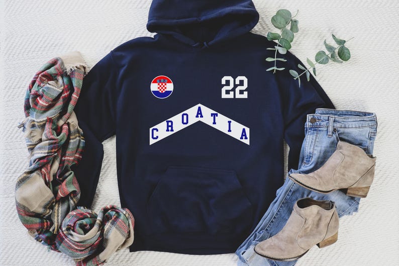 Pu&ograve; includere: Una felpa con cappuccio blu navy con un design a chevron bianco che dice "CROATIA" e il numero "22". La felpa presenta anche una bandiera croata rossa, bianca e blu.