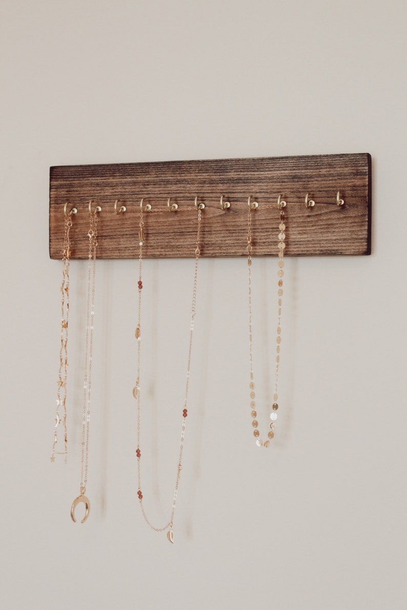 May include: A wooden jewelry organizer with gold hooks, holding several gold necklaces with different pendant styles.