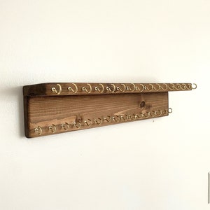 May include: A wooden key holder with a shelf and multiple gold hooks. The key holder is mounted on a white wall.