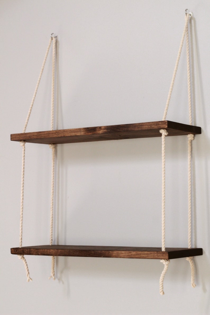 May include: Two wooden shelves hanging from the ceiling with white ropes. The shelves are stained a dark brown colour.