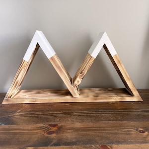 May include: A wooden shelf in the shape of two triangles with white painted tops. The shelf is made of natural wood with a rustic finish.