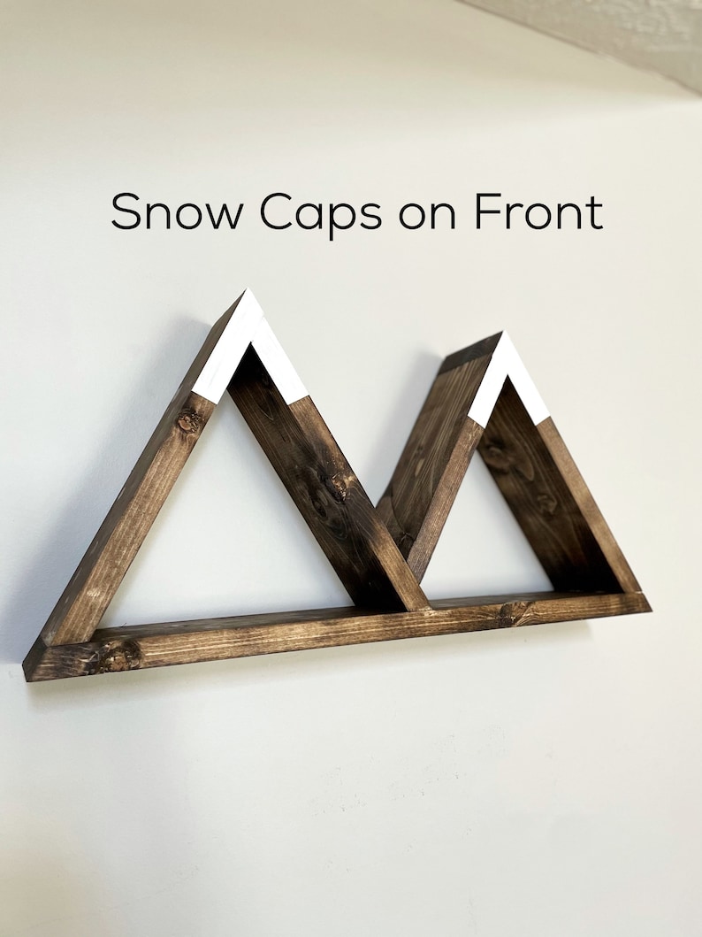 May include: A wooden shelf shaped like two mountains with white snow caps on top. The shelf is mounted on a white wall. "Snow Caps on Front" is written above the shelf.