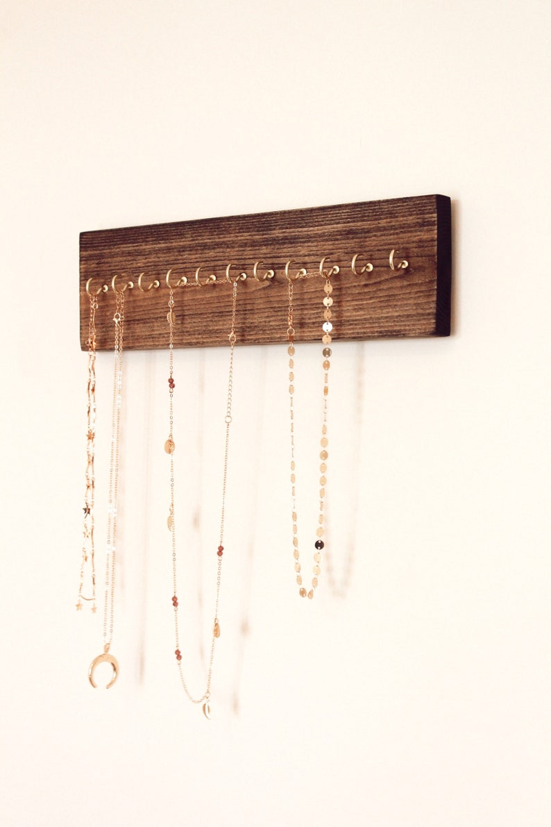 May include: A dark brown wooden jewelry organizer with gold hooks. Five gold necklaces are hanging from the hooks.