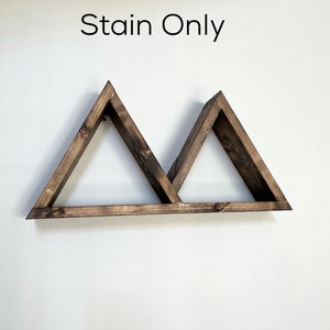 May include: A wooden shelf with two triangular shelves, stained in a dark brown colour. The shelf is mounted on a white wall and the text "Stain Only" is written above the shelf.