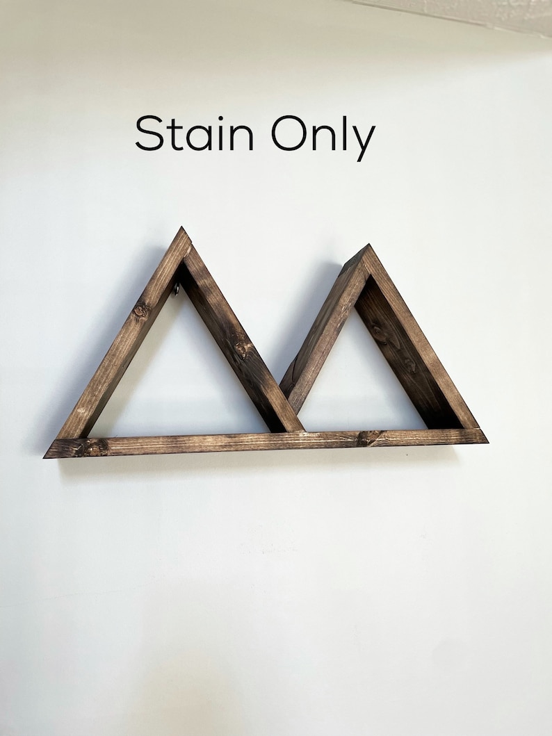 May include: A wooden shelf with two triangular shelves, stained in a dark brown colour. The shelf is mounted on a white wall and the text "Stain Only" is written above the shelf.