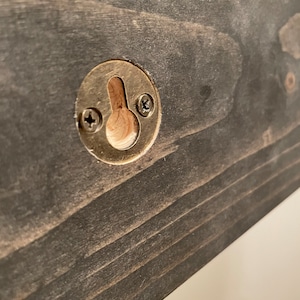 May include: A close-up of a dark wood shelf with a brass hanging hook. The hook has two screws securing it to the shelf.