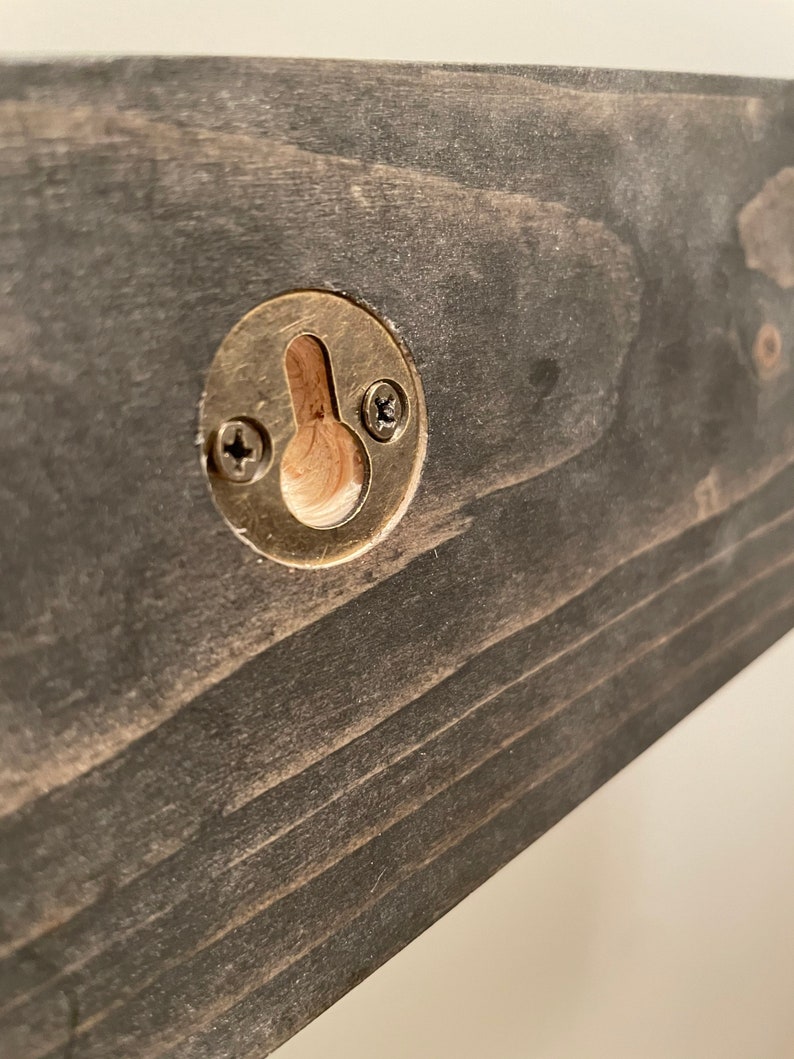 May include: A close-up of a dark wood shelf with a brass hanging hook. The hook has two screws securing it to the shelf.