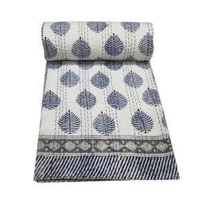 Pode incluir: Um edredom branco e azul marinho enrolado com um padrão de folhas. O edredom apresenta um padrão repetido de folhas azul marinho sobre um fundo branco, com uma borda decorativa e uma borda listrada.