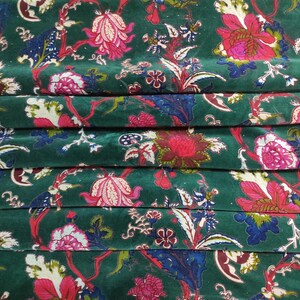 May include: Close-up of a folded fabric with a dark green background. The fabric features a floral pattern with pink, red, white, and blue flowers and leaves. The design is repeated across the fabric.