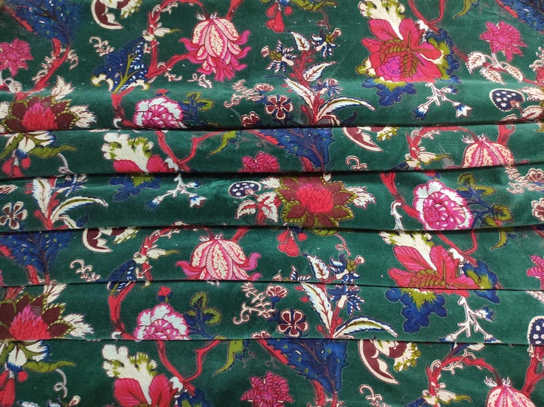 May include: Close-up of a folded fabric with a dark green background. The fabric features a floral pattern with pink, red, white, and blue flowers and leaves. The design is repeated across the fabric.