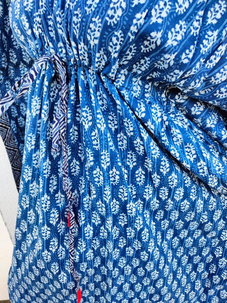 May include: A blue and white patterned cotton dress with a drawstring waist. The dress has a floral design and a tie at the waist.